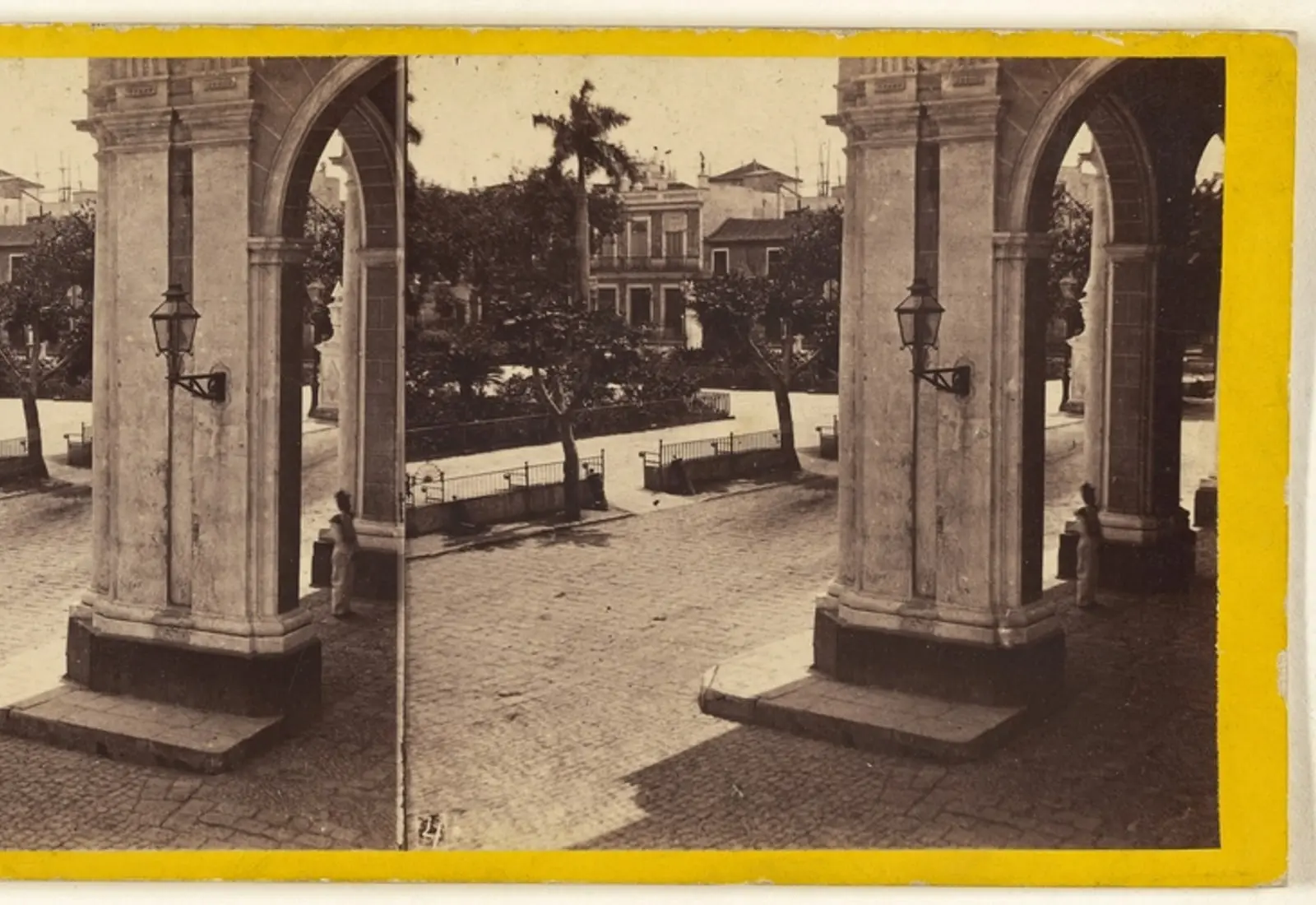 Fotografía antigua en sepia de una plaza habanera con un arco de piedra